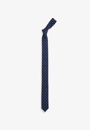 Cravate marine avec des pois blancs, fabriquée en tissu texturé. Présente une extrémité pointue et un nœud en haut, adaptée aux occasions formelles.