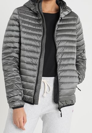 Person wearing an unzipped gray quilted hooded jacket over a black shirt and light gray sweatpants with a white drawstring.