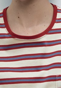 Niska ja ylävartalo, joissa päällä kerma-valkoinen paita, jossa punaiset ja siniset vaakaraitat sekä punainen pääntie.