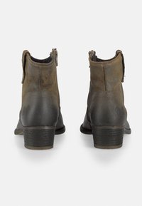 Botas de tobillo de ante marrón con tacón de cuero negro, cierre de cremallera y textura suave. Presenta un pequeño logo en el lateral y un diseño curvado.