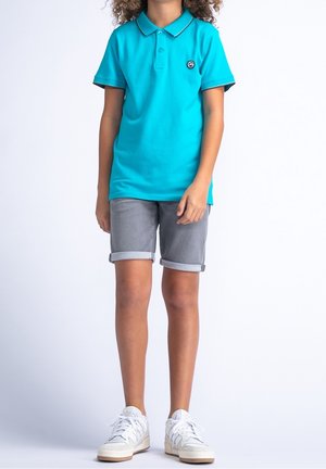 Turquoise poloshirt met een kraag, grijze opgerolde shorts en witte sneakers. Bevat een klein rond logo op het shirt.