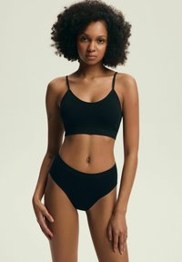 Czarny biustonosz typu bralette z cienkimi ramiączkami oraz wysokim stanem czarne majtki, obie części wykonane z gładkiego materiału. Prosty design, minimalne ozdoby.