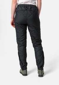 Pantalons isolés noirs avec un motif à losanges, taille élastique, zips latéraux et jambes fuselées, associés à des chaussures vertes imperméables.