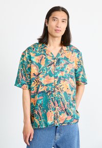 Short-sleeve button-up shirt featuring a vibrant green fabric with abstract orange and black patterns, complemented by a relaxed fit and collar.