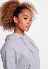 Haut gris clair en mélange de coton, équipé d'une poche avant, d'une capuche avec cordon de serrage et d'un petit logo blanc sur la poitrine à gauche.