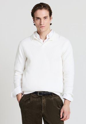 Maglione bianco a coste con colletto, abbinato a pantaloni in velluto a coste di colore verde scuro. Tessuto leggero, vestibilità casual e dettaglio dei polsini visibile.