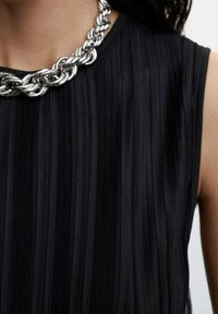 Top nero a coste senza maniche con una collana in argento spesso. La texture è liscia, con strisce verticali che aggiungono profondità.