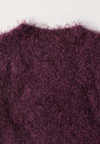 Gros plan d'un col de pull doux, duveteux et violet foncé avec un tissu tricoté texturé et poilu sur un fond uni.
