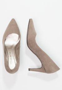 Beżowe zamszowe szpilki z szpiczastym noskiem, srebrną podszyciem oraz smukłym, 8-centymetrowym obcasem typu szpilka. Posiadają boczne wycięcie.