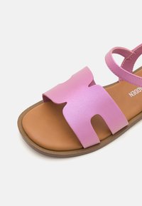 Rosa sandal med en matt remdesign, en urtagning och en brun texturerad sula. Justerbar rem för en säker passform.