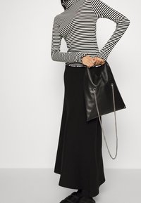 Gestreepte coltrui, zwart-wit, aansluitende mouwen; lange zwarte rok; zwarte leren tas met kettingband en driehoekige vorm.