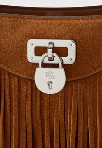 Pruun seemisnahast käekott, millel on vertikaalsed tutid, hõbedane lukustus graveeritud initsiaalidega ja sile sisevooder.