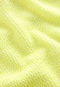 Tekstūruota medžiaga ryškiai geltonos spalvos su banguotu raštu, turinti iškilusias banguotas kraštines ir minkštą, šiek tiek blizgančią apdailą.