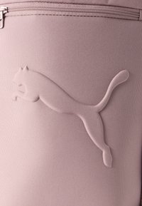 Ροζ ύφασμα με υφή που έχει ανάγλυφο, στυλιζαρισμένο λογότυπο πηδιχτής γάτας. Περιλαμβάνει λεπτομέρεια με φερμουάρ κλεισίματος.