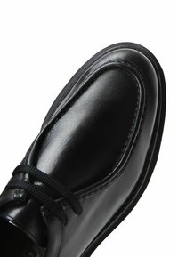 Zwarte leren schoen met een gladde textuur, ronde neus, stoffen veters en gedetailleerde stiksels langs de randen en rondom de opening.