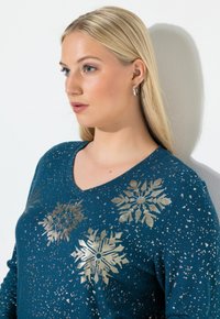 Tealowy sweter z dekoltem w kształcie litery V, ozdobiony złotymi wzorami płatków śniegu, o teksturze w drobne kropki, z długimi rękawami i luźnym krojem. Idealny na zimowe dni.
