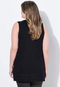 Top nero senza maniche con vestibilità rilassata, realizzato in un tessuto leggero. I dettagli notevoli includono un colletto arrotondato e un orlo posteriore più lungo.