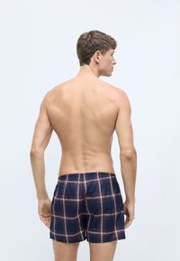 Pantaloni da bagno a quadretti con base blu navy, impreziositi da linee rosse e bianche. Vita elasticizzata, lunghezza a metà coscia, materiale in cotone. Vista posteriore mostrata.