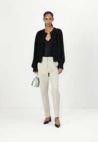 Fekete bolyhos kardigán két gombbal, fekete camisole top, világos bézs szabott nadrág, és fényes fekete magassarkú cipő. Ezüst kézitáska zsinórral.