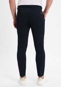 Navy Slim-Fit-Hosen aus strukturiertem Material, mit zwei Gesäßtaschen, einem Bund mit Gürtelschlaufen und schmal zulaufenden Knöcheln, kombiniert mit hellen Sneakers.