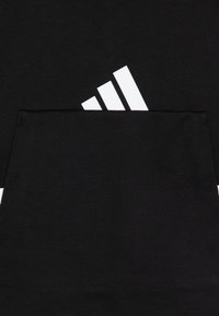 Svart stoff med en stor hvit Adidas-logo og tre striper på toppen. Teksturen er glatt og matt, uten noen ekstra mønstre.