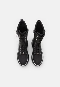 Botas negras con cordones que presentan un exterior de tela suave, acentos de hardware plateado, punta redonda y suelas blancas con un detalle mínimo.