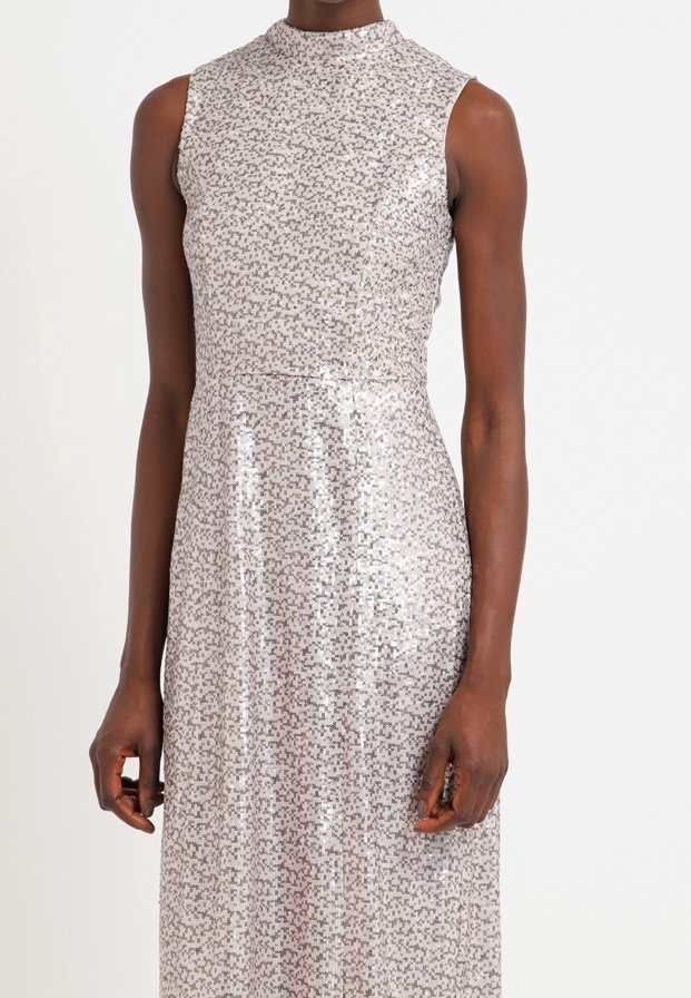 Vestido sin mangas de lentejuelas plateadas con cuello alto, corpiño ajustado y falda línea A, llevado por una persona con tono de piel oscura.