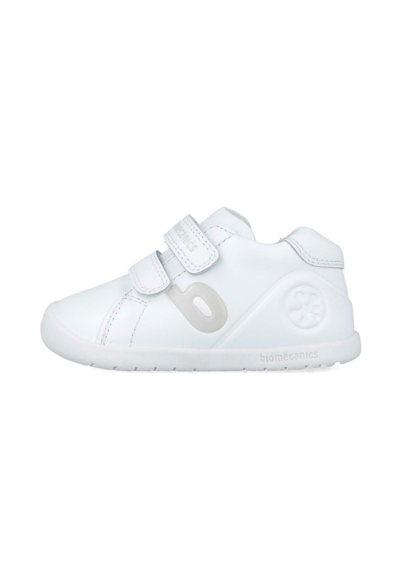Zapatilla infantil blanca con parte superior de cuero liso, dos tiras de Velcro, forma redondeada y suela de goma texturizada. Logotipo de la marca en el lateral.