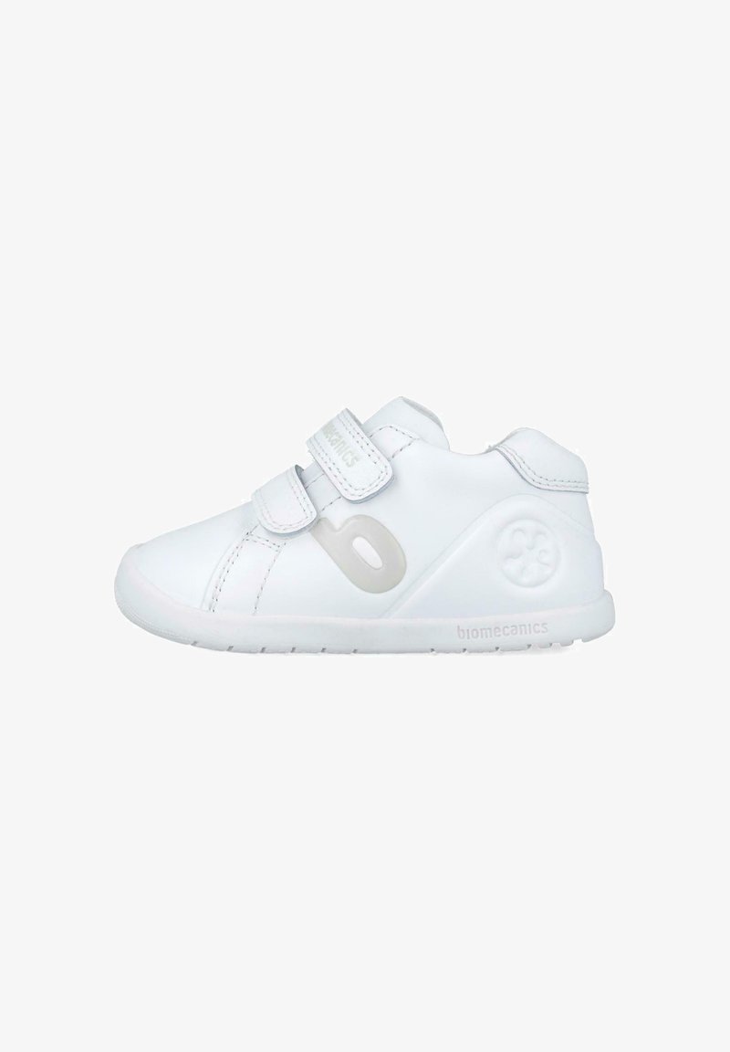 Zapatilla infantil blanca con parte superior de cuero liso, dos tiras de Velcro, forma redondeada y suela de goma texturizada. Logotipo de la marca en el lateral.