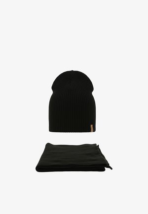 Zwarte geribbelde gebreide muts met klein beige label, gecombineerd met een opgevouwen zwarte fleece sjaal op een witte achtergrond.