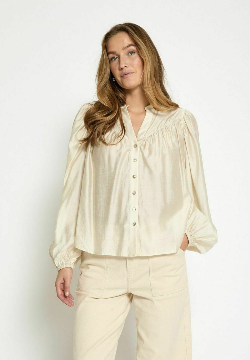 Cream, long-sleeve blouse with button-down front, pleated shoulder detail, and gathered cuffs, made of a smooth, lightweight fabric.