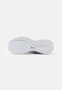Semelle de chaussure de sport blanche, présentant un motif de grip texturé avec des formes hexagonales, un détail de logo et une construction légère et flexible.