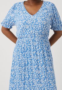 Vestido azul con estampado floral, mangas cortas con volumen, cuello en V y cinturilla elástica. Patron de flores blancas en todo el vestido. Detalle de botones en la parte delantera.