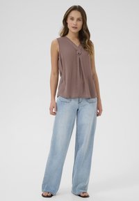 Mouwloze mauve top met een v-hals en knoopdetail, gecombineerd met lichtblauwe wijde jeans. Zachte textuur en relaxed fit.