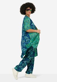 Printed blue and green outfit featuring a loose top with short sleeves and matching pants. Accompanied by white sneakers and reflective sunglasses.
