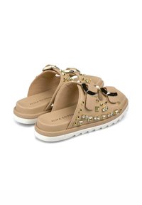 Sandales à glissière beiges avec des clous dorés et des strass, une semelle plate avec un bord blanc, et deux brides pour un maintien sécurisé.