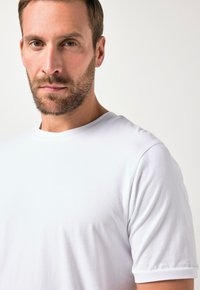 Camiseta de algodón blanca con cuello redondo y mangas cortas, con una textura suave y un ajuste relajado. Diseño simple y sin adornos.