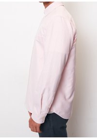 Chemise à manches longues rose à rayures blanches, avec un col boutonné, une poche poitrine, et des boutons sur les poignets et l'ourlet.