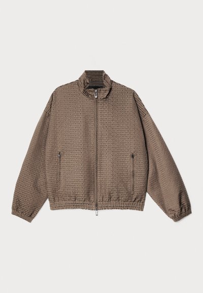 Light brown zip-up jacket with a textured pattern. Features a high collar, elastic cuffs, and two zipped side pockets.