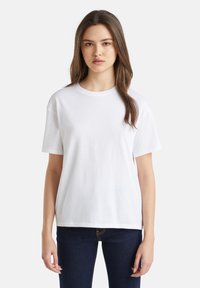 Witte katoenen t-shirt met een ronde hals en korte mouwen. Loose fit, gladde textuur en een eenvoudig ontwerp. Draagt met donkere jeans.