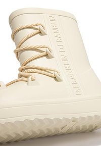 Bota de goma marfil con cordones color crema, suela texturizada y nombre de la marca en relieve en el lateral. Diseño impermeable para mayor durabilidad.