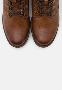 Bocanci din piele maro cu o suprafață texturată, dotati cu șireturi gri, ochiuri de metal și o talpă de cauciuc rezistentă, priviți dintr-o parte.