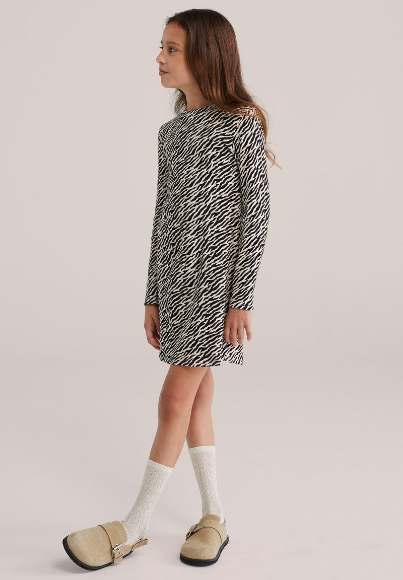 Hosszú ujjú ruha fekete-fehér csíkos mintával, térd alá érő hosszúságban, világos bézs klumpákkal és fehér mintás térdzoknival párosítva.