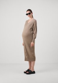 Beige színű kötött, bordás midi ruha V-nyakkal és hosszú ujjakkal. Fekete platform slip-on cipőkkel viselve. Simább textúra, laza szabás.