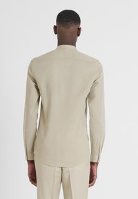 Camicia a maniche lunghe beige chiaro realizzata in tessuto morbido. Presenta un colletto alla cinese, orlo curvo e polsini con bottoni. Design minimalista.