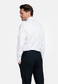 Witte dress-shirt met donkere knoopaccenten, gecombineerd met een donkere broek. Gladde stof; fitted design met een klassieke kraag en een rugplooi.