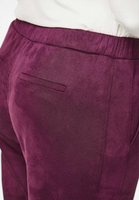 Pluche, diep paarse broek met een elastische tailleband, met een enkele achterzak en een gladde textuur. Subtiele glans over de stof.