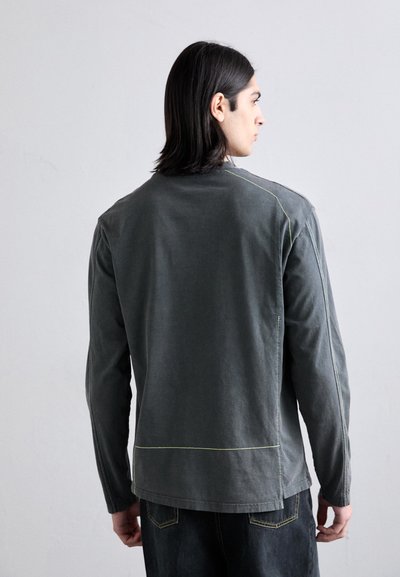 Chemise grise à manches longues en coton avec des accents de couture jaune, coupe décontractée et col rond, vue de dos.