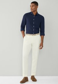 Námornícko modrá košeľa s krátkymi rukávmi, skombinovaná s krémovými nohavicami a hnedými semišovými šnurovacími topánkami. Minimalistický štýl a neutrálne farby.