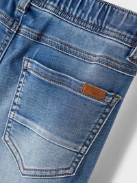 Jeans in denim di un azzurro chiaro, con un elastico arricciato in vita, una sola tasca posteriore e un piccolo etichetta del marchio marrone.